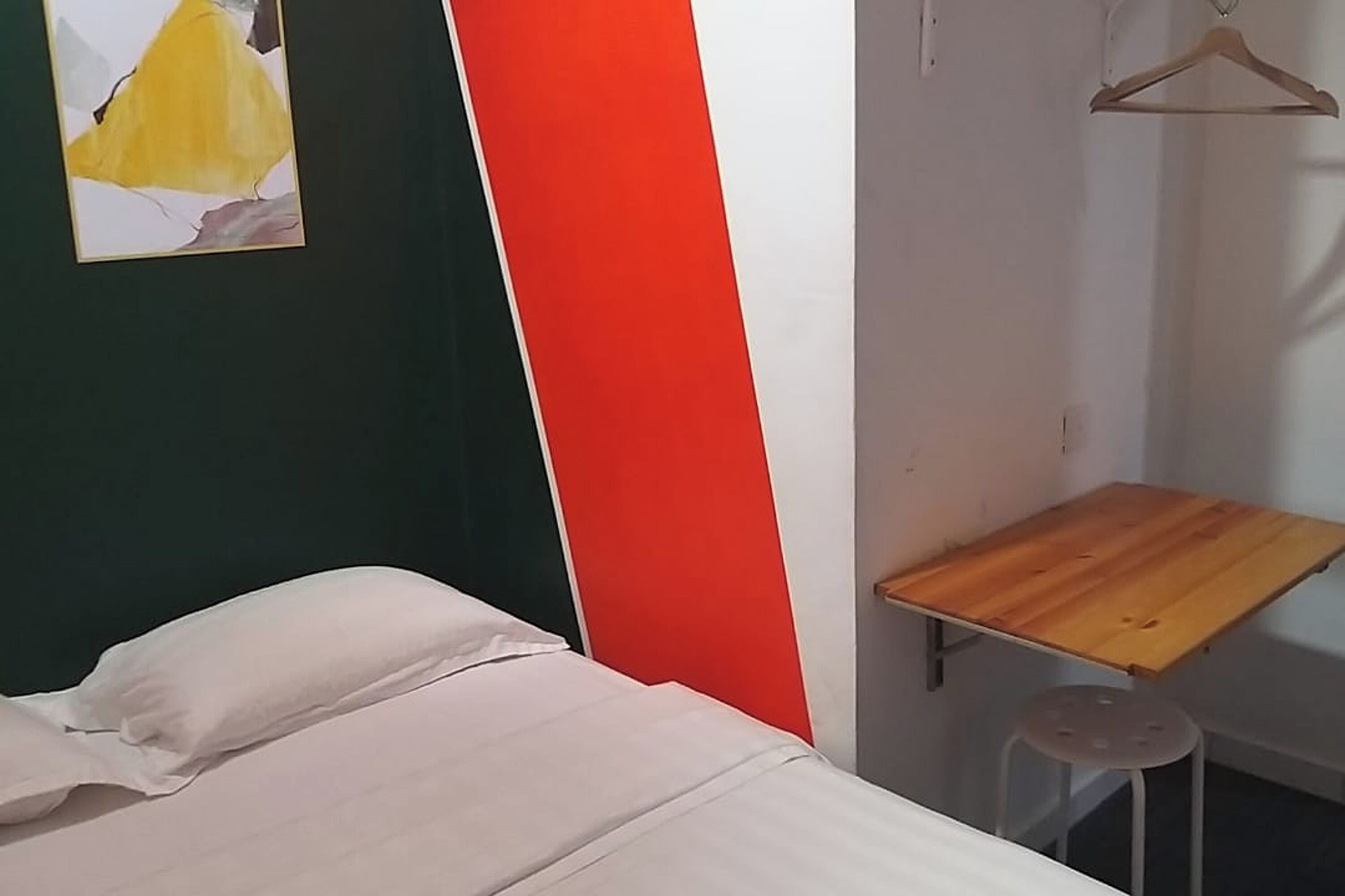 A bed with white bedding, a small wooden table, and a hanging wooden hanger.