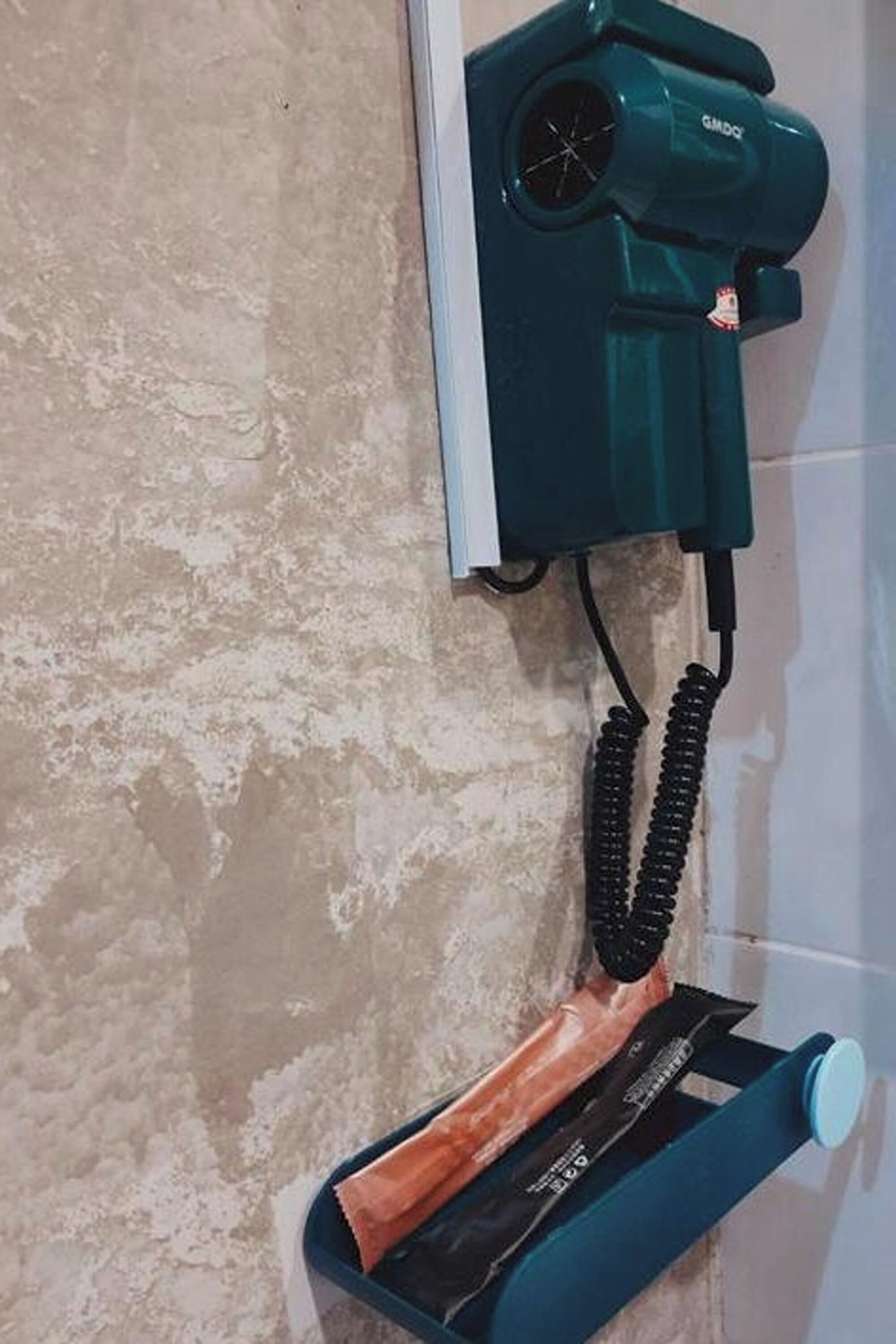 A hairdryer mounted on a textured wall, a coiled power cord, and a blue towel rack with a towel.