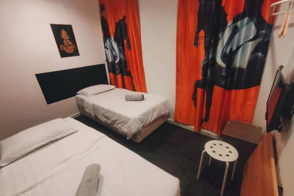 Ein Zimmer mit zwei Betten, einem kleinen Tisch und orangefarbenen Vorhängen mit schwarz-weißen Mustern.