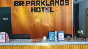 A reception desk at BR Parklands Hotel with a vertical orange panel, a digital screen, and various informational brochures and a QR code.