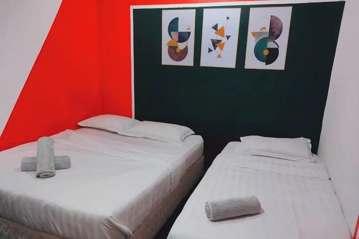 Una habitación con dos camas, cada una con una almohada y una toalla enrollada. Hay obras de arte abstractas en la pared sobre las camas.