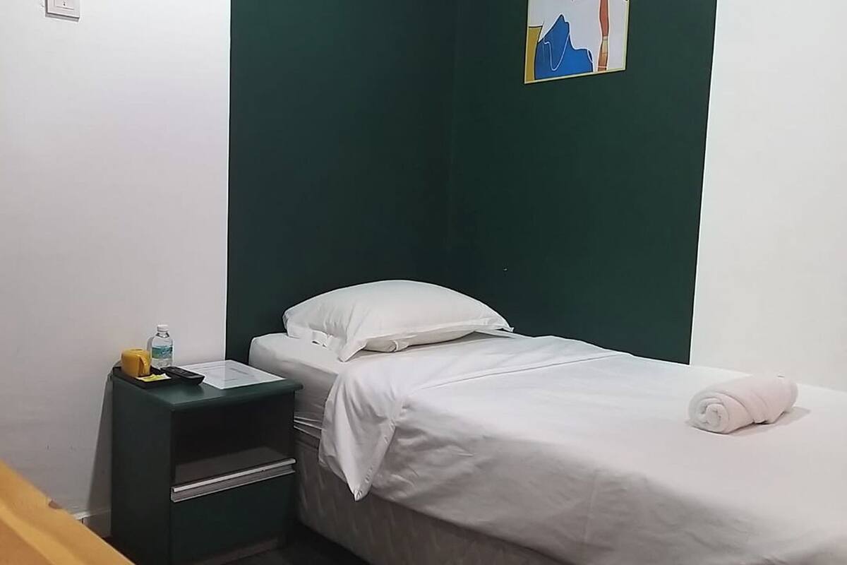 Ein kleiner, ordentlicher Raum mit einem Einzelbett, einem Nachttisch und einem an der Wand hängenden Gemälde.