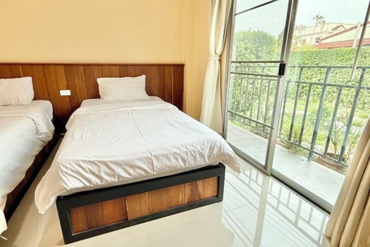 A hotel room with two beds, a balcony with a metal railing, and a view of greenery outside.