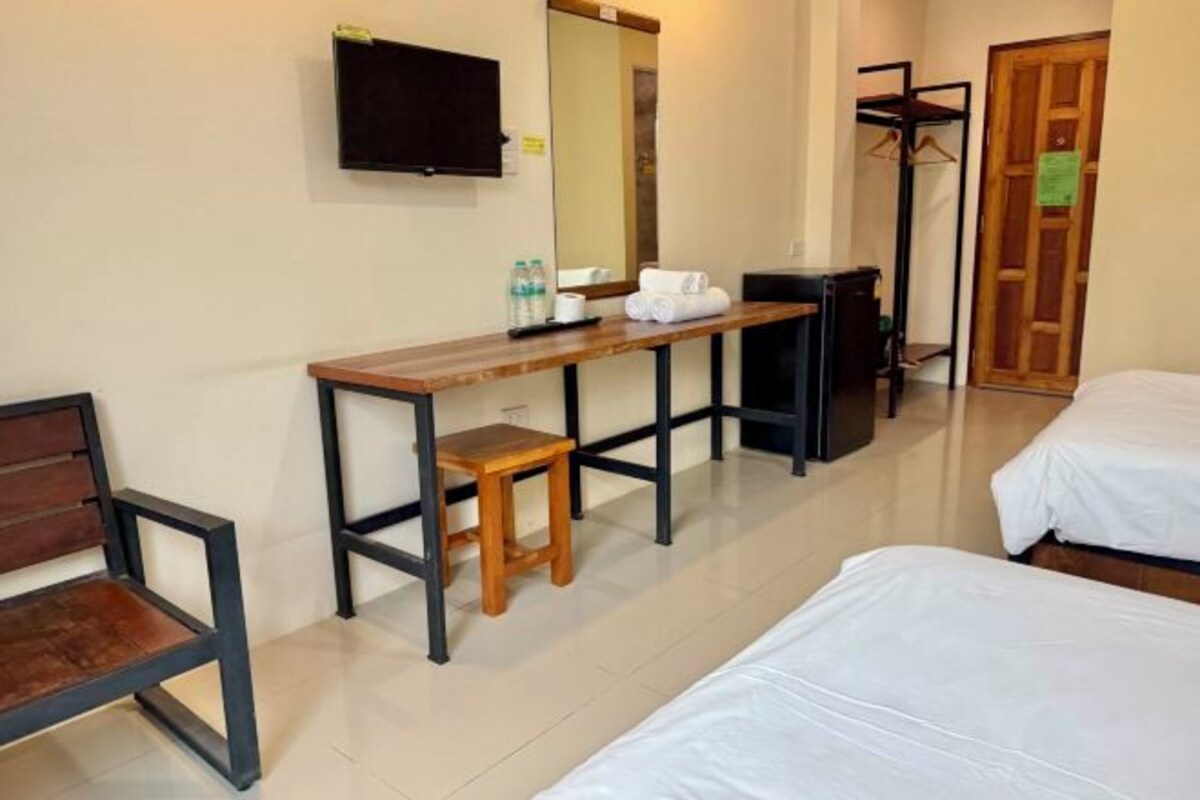 A hotel room with a wooden desk, a chair, a bed, a TV, and a wardrobe.