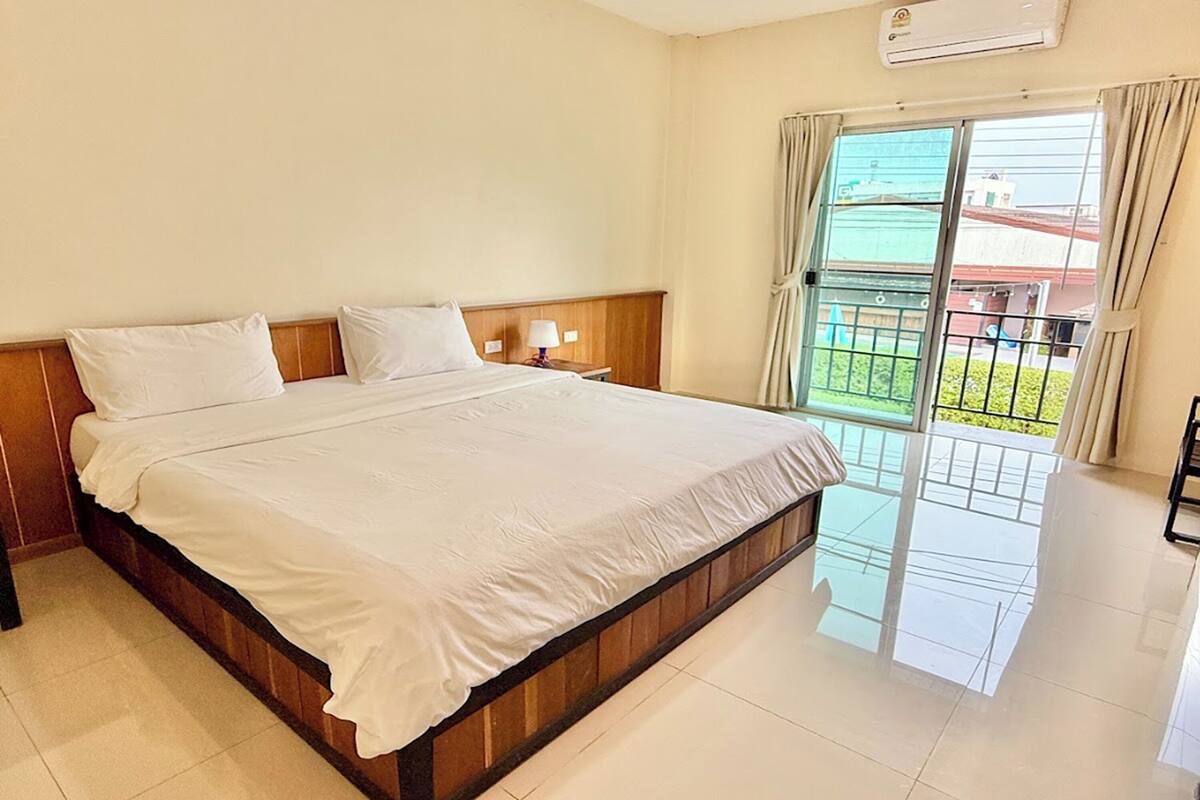 A hotel room with a large bed, a nightstand, a lamp, and a view of the outside balcony.