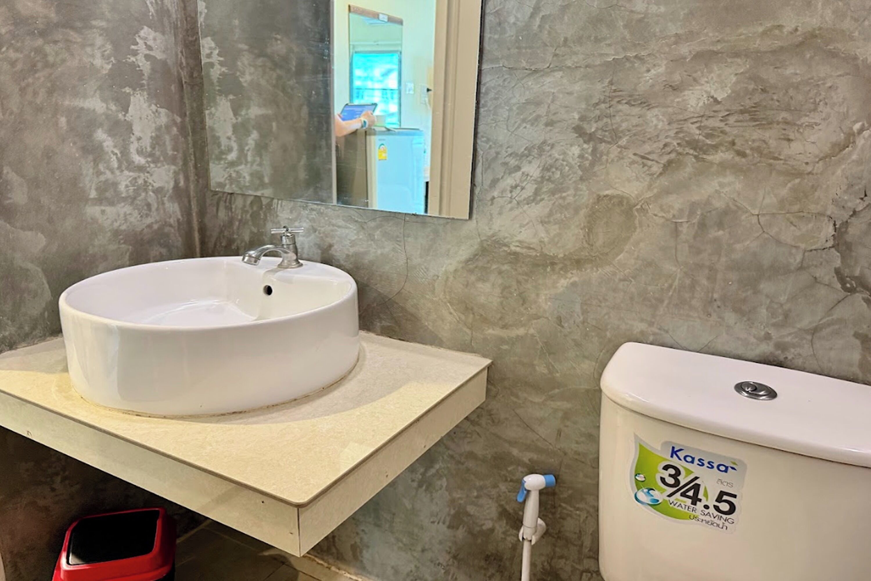A bathroom with a white sink, a mirror, and a toilet with a water-saving label.