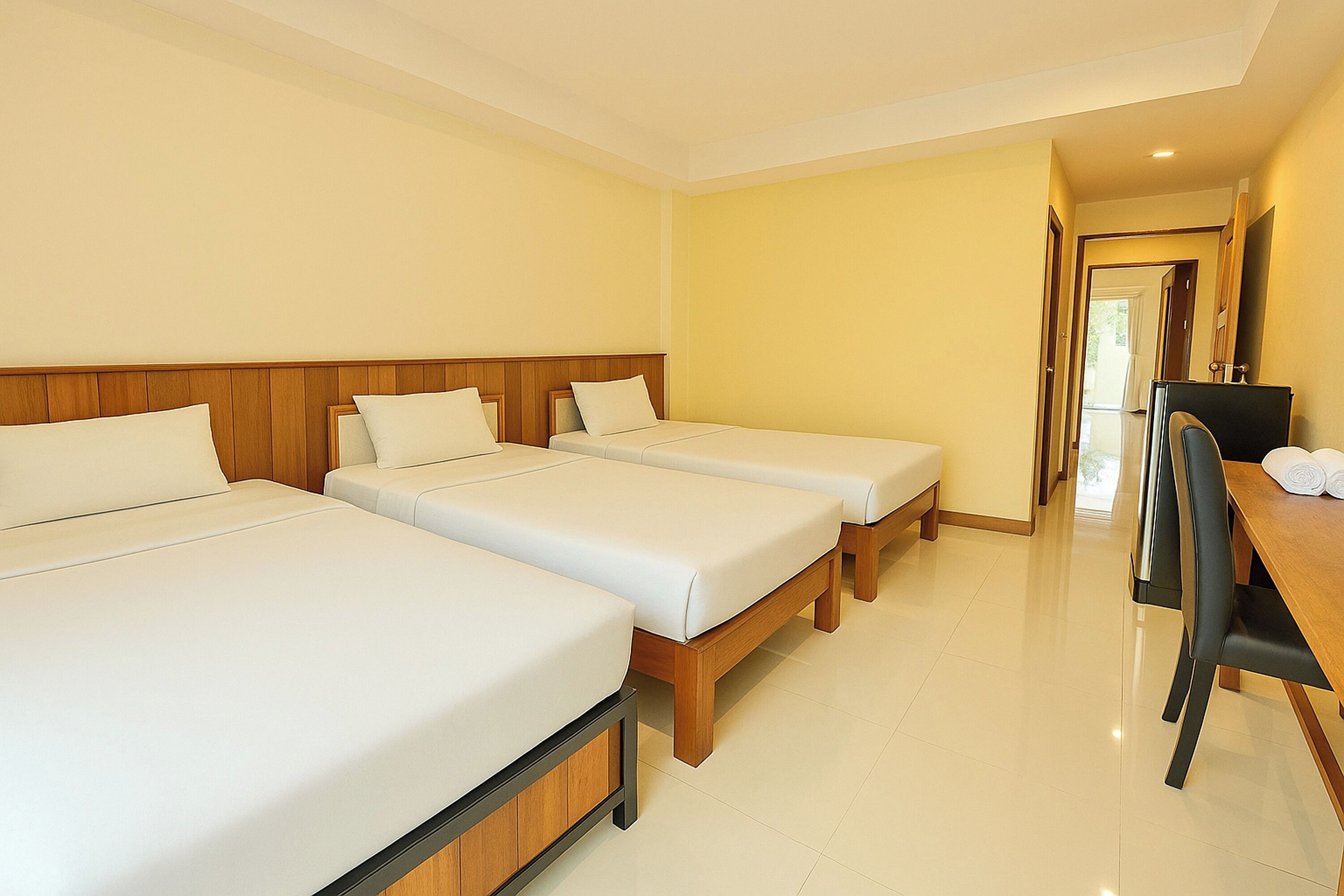 A hotel room with three single beds, a wooden desk with a chair, and a door leading to another room.