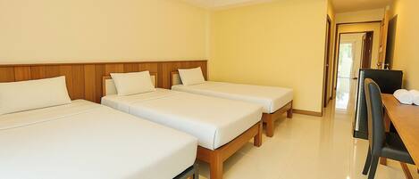 A hotel room with three single beds, a wooden desk with a chair, and a door leading to another room.