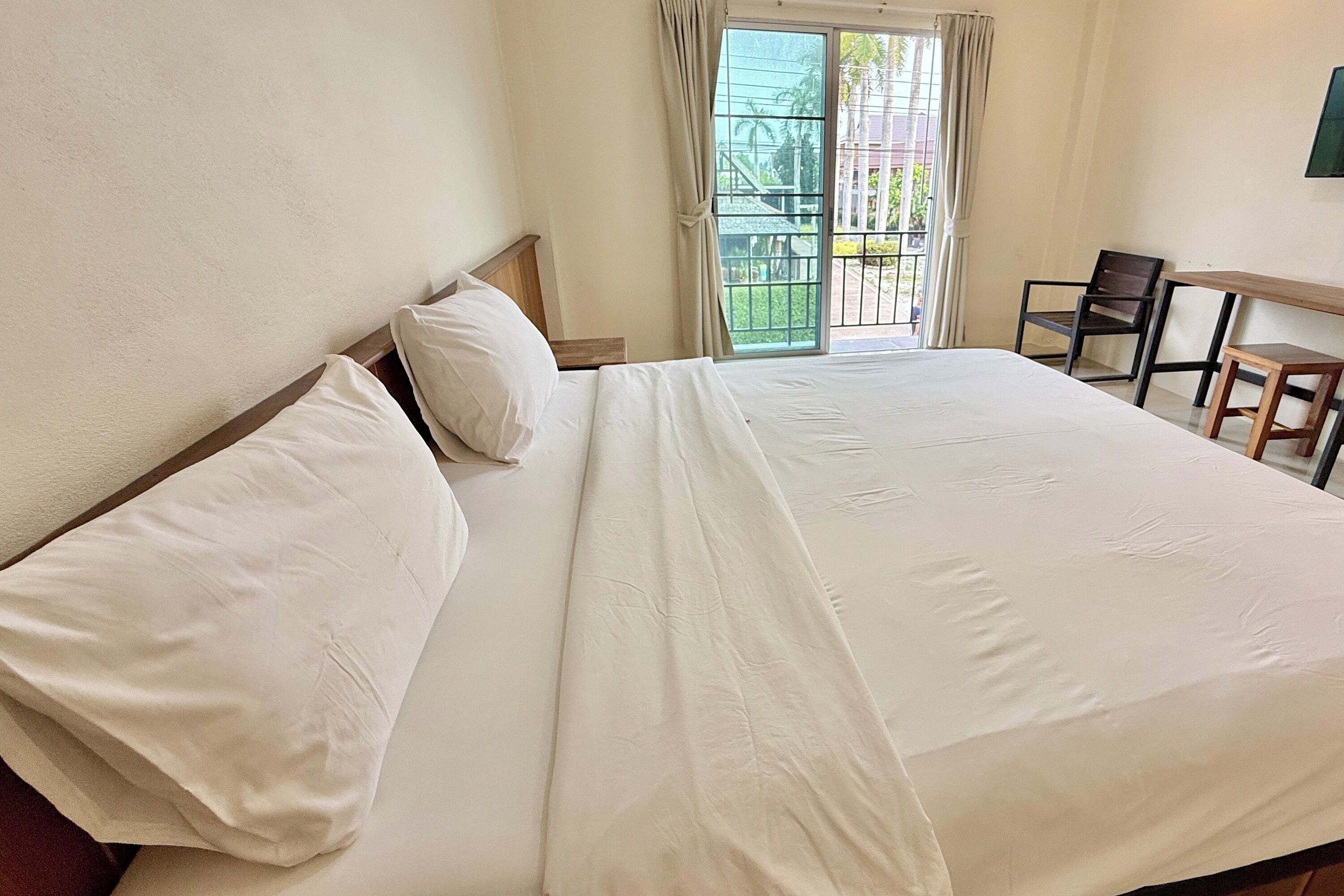 Habitación de hotel con una cama grande, una mesita de noche de madera, una pequeña mesa con una silla y vistas al balcón exterior.
