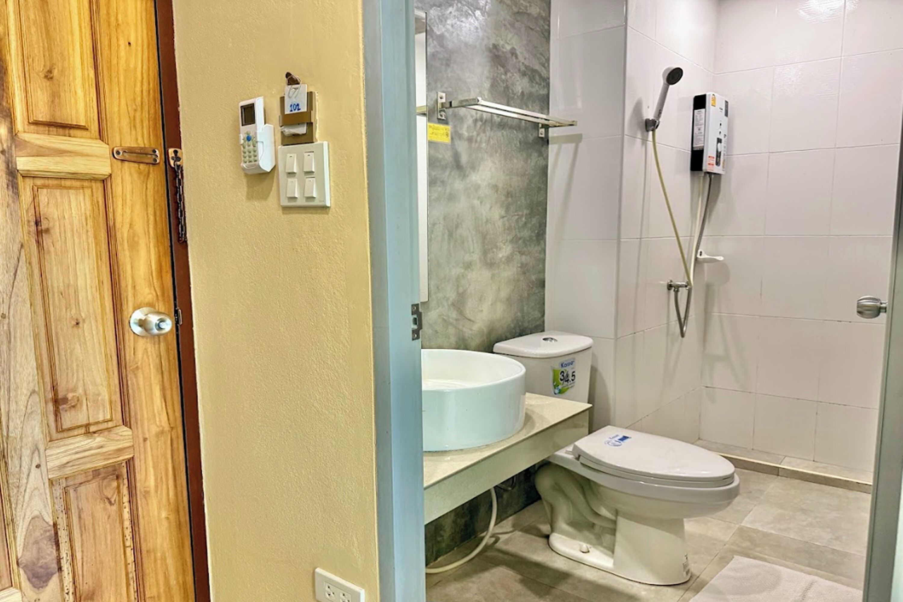 A bathroom with a wooden door, a white toilet, a sink with a marble countertop, and a shower with a handheld showerhead.