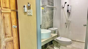 A bathroom with a wooden door, a white toilet, a sink with a marble countertop, and a shower with a handheld showerhead.