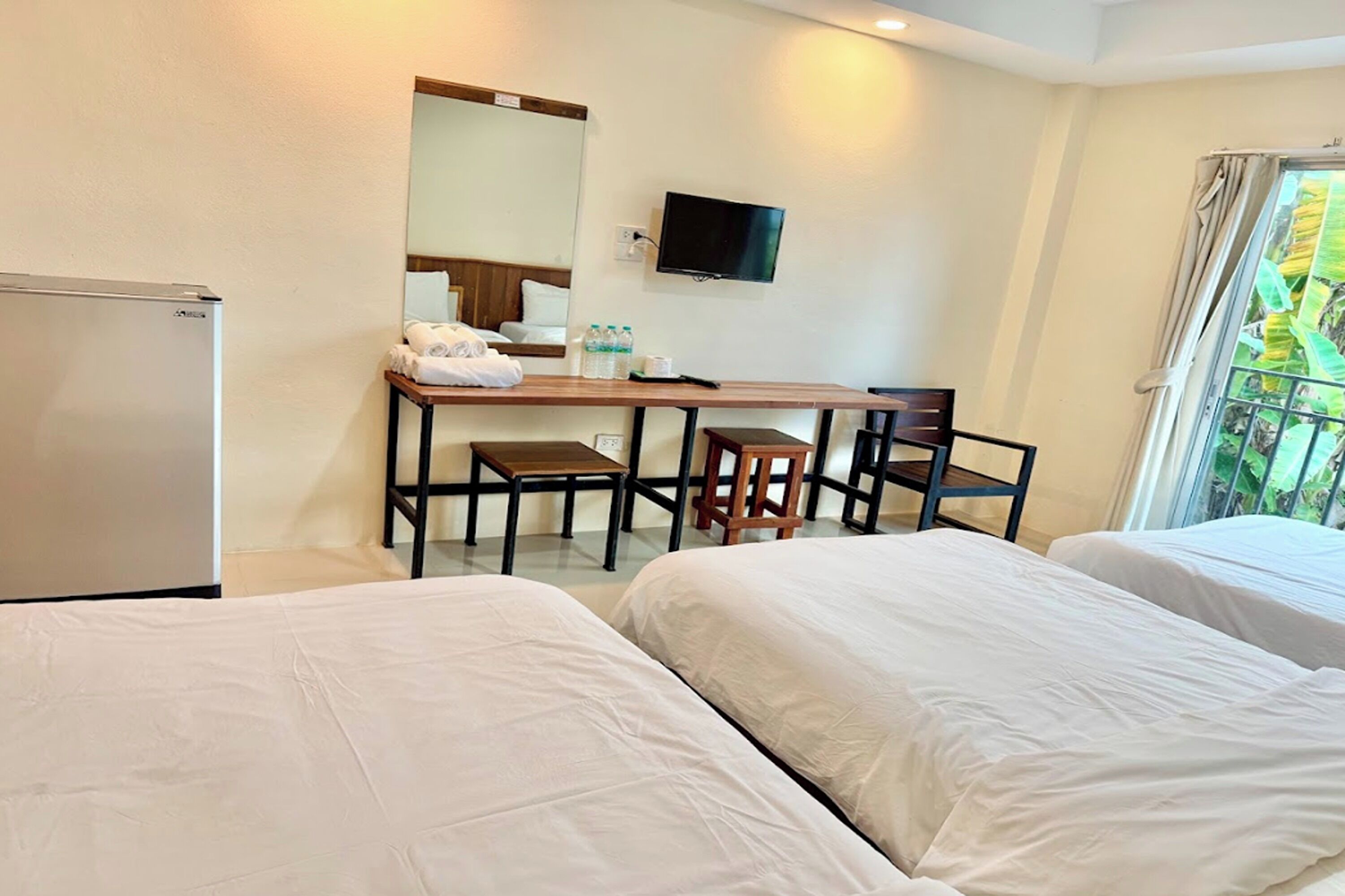 A hotel room with two beds, a desk with a chair, a TV, and a window with curtains.