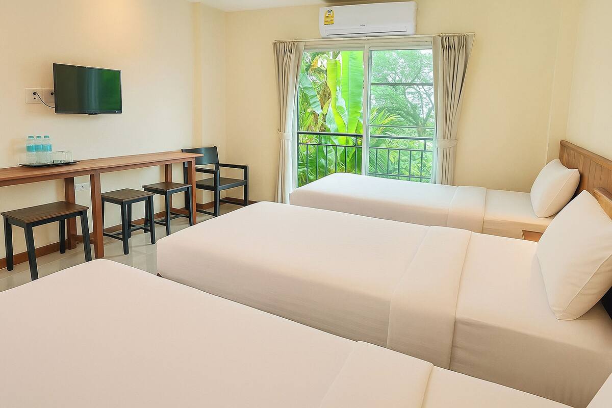 A hotel room with two beds, a desk with chairs, a TV, and a window with curtains.