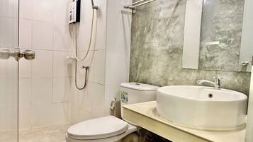 A bathroom with a toilet, a sink, a shower, and a mirror.