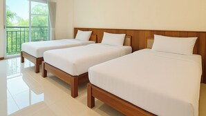 Une chambre d’hôtel avec trois lits simples, un balcon donnant sur un espace verdoyant et une grande fenêtre.