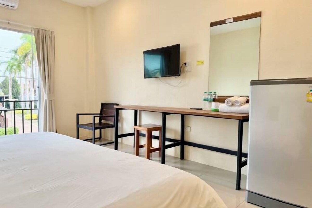 A hotel room with a bed, a desk with a chair, a television mounted on the wall, a refrigerator, and a window with curtains.