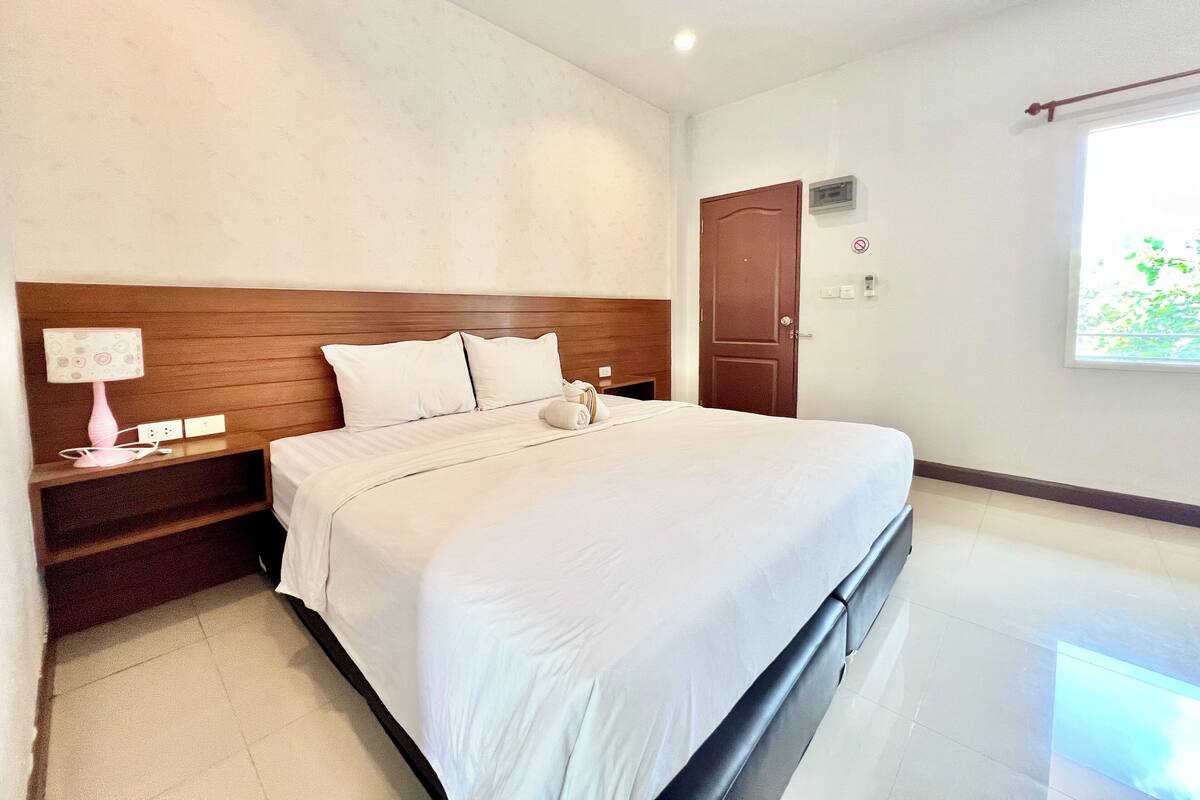 Una habitación de hotel con una cama grande, un cabecero de madera, una mesita de noche con una lámpara y una puerta con ventanal.