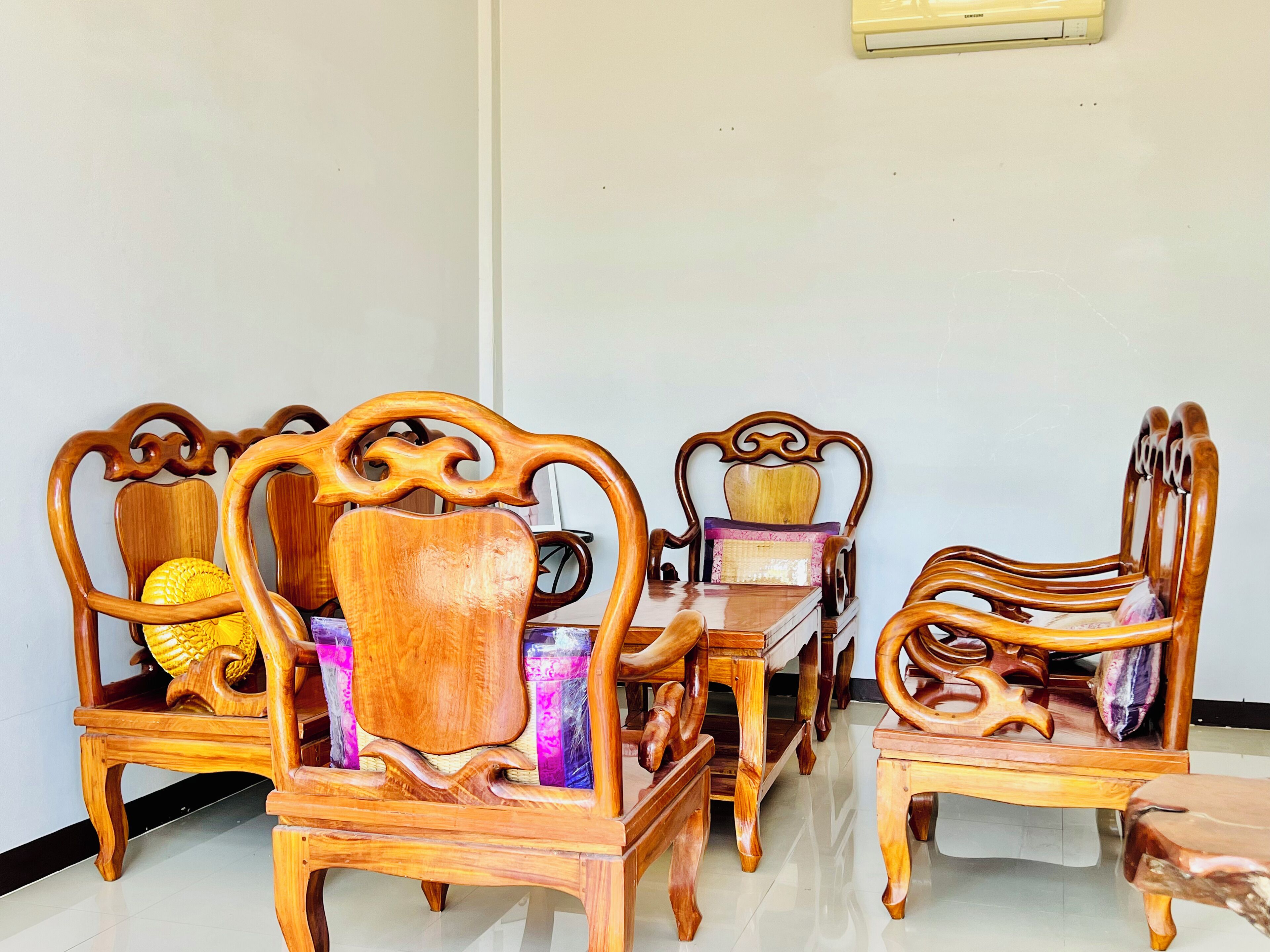 A dining set with ornate wooden chairs and a table, featuring a decorative cushion and a woven basket.