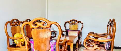 Un juego de comedor con sillas de madera ricamente decoradas y una mesa, que incluye un cojín decorativo y una cesta tejida.
