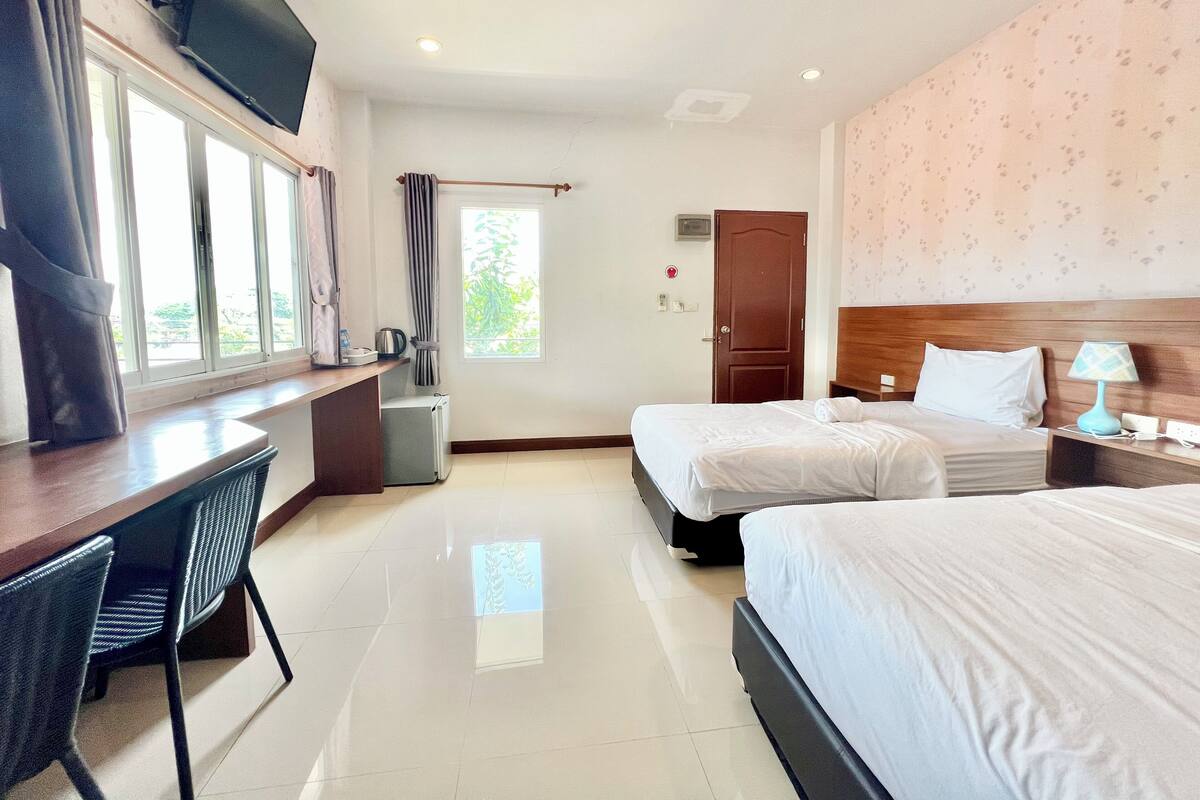 Una habitación de hotel con dos camas, un escritorio, una silla, un televisor y una ventana con cortinas.
