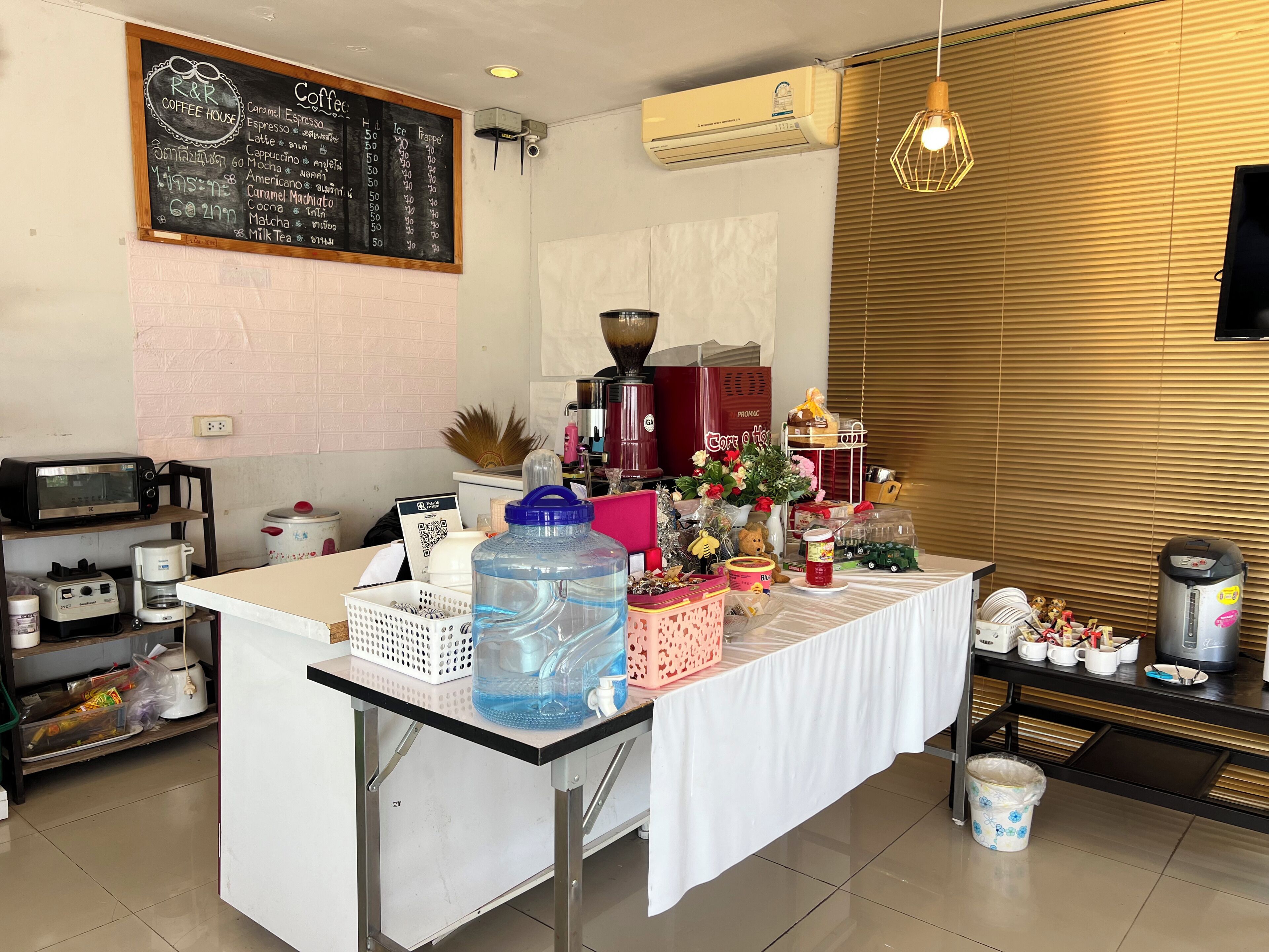 A coffee shop counter with a menu, coffee machines, and various items on the counter.
