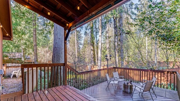 Una terraza de madera con mobiliario exterior, rodeada de un área boscosa.
