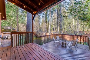 A wooden deck with outdoor seating, surrounded by a forested area.