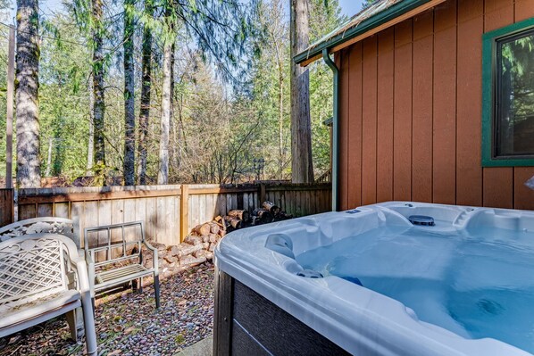A hot tub in a backyard with a wooden deck, a metal bench, and a wooden fence.
