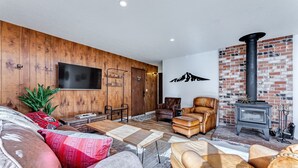 Una sala de estar acogedora con pared de madera, sofás de cuero, un televisor y una chimenea de ladrillo.