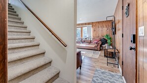 Una escalera conduce a una sala de estar con piso de madera, un sofá y una mesita de centro.