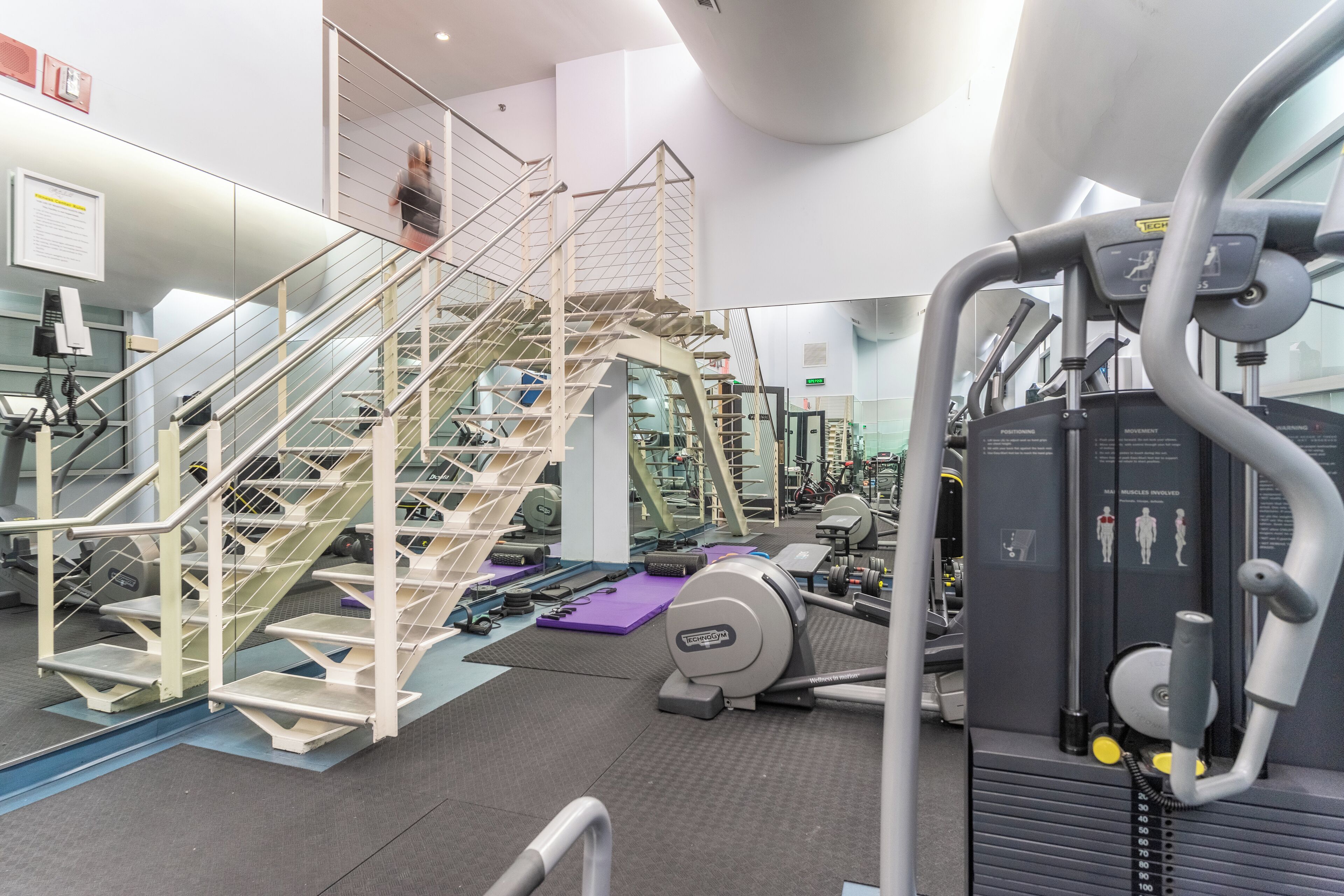 Een fitnessruimte met een trap, trainingsapparatuur en een spiegelwand.