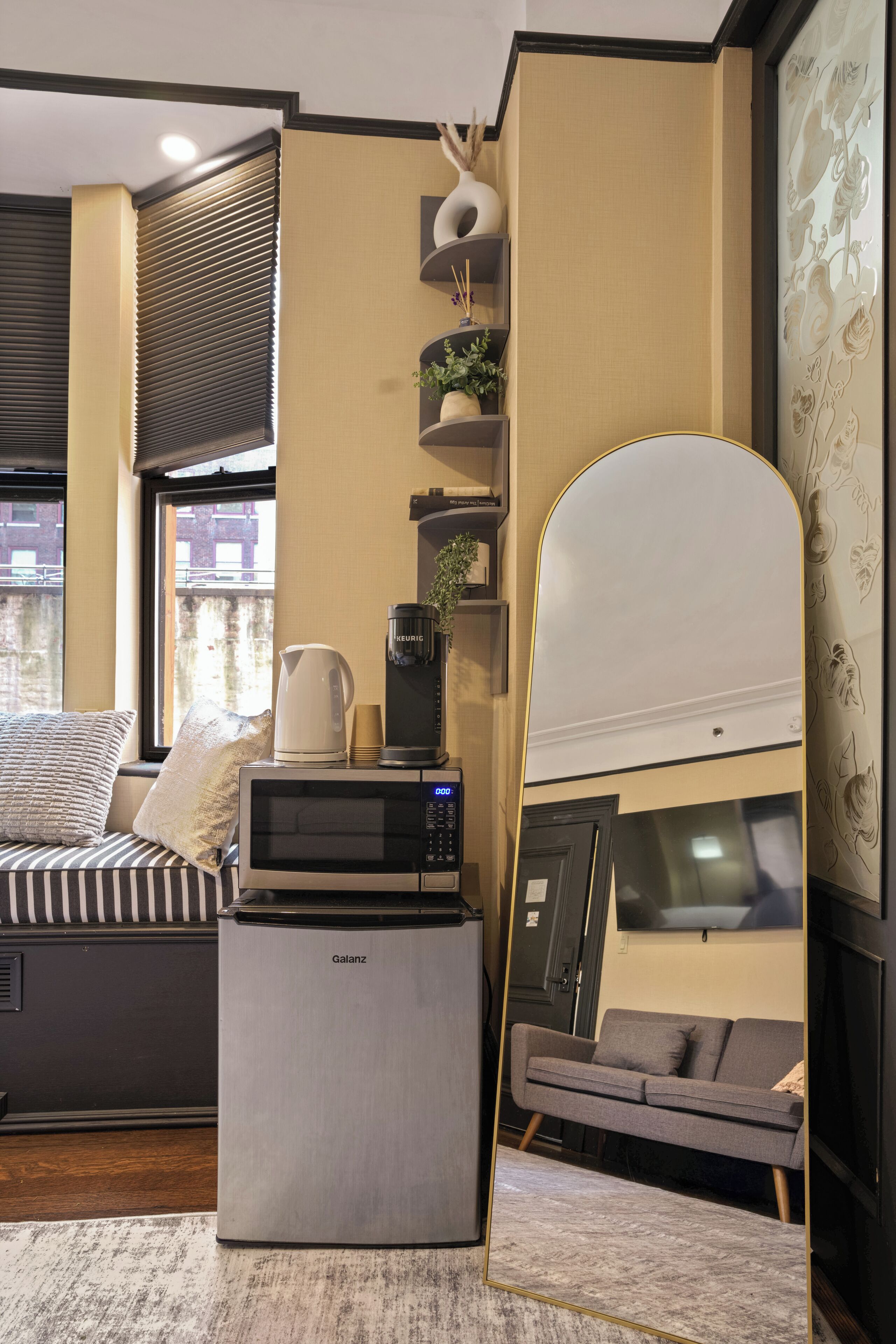 A compact living space with a sofa, a coffee maker, a microwave, and a large mirror.