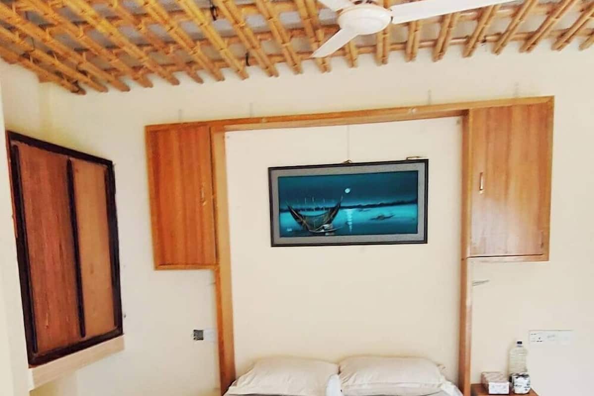 Un dormitori amb un llit gran, un ventilador de sostre, una nitòria i un quadre a la paret.