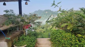 Un sendero que lleva a una vista de la montaña, rodeado de abundante vegetación y un edificio rústico con techo de paja.