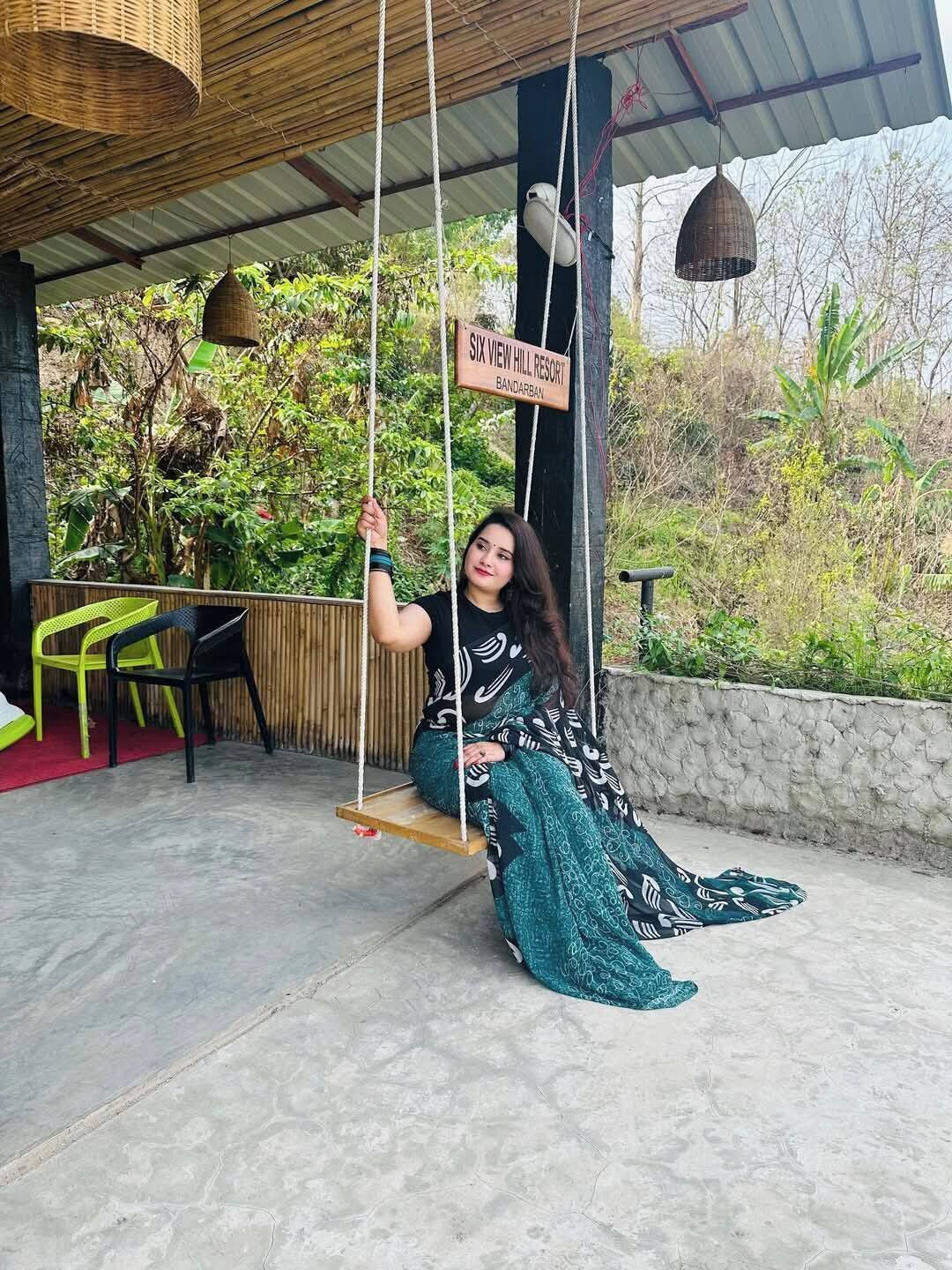 A person sitting on a swing under a covered area with a sign reading "SIX VIEW HILL RESORT BANDARBAN".
