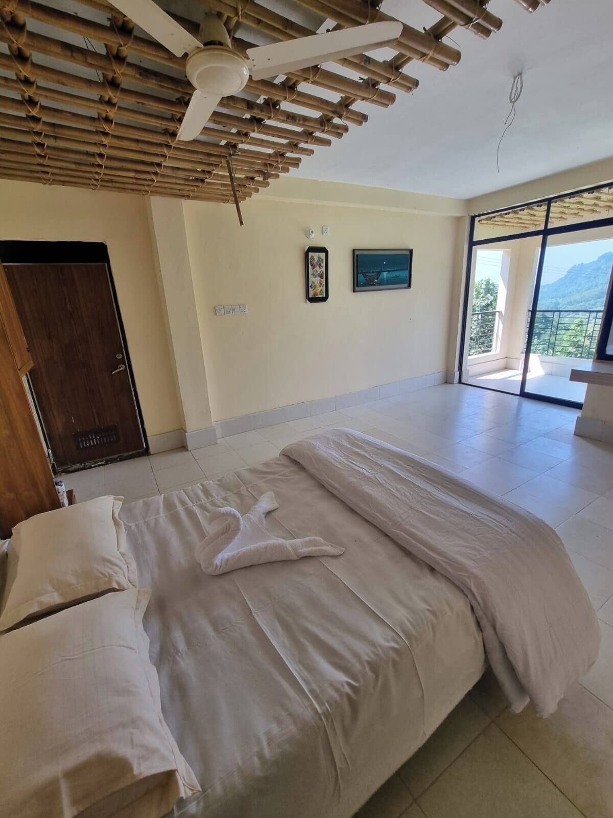 Een slaapkamer met een bed, een houten plafond, een deur en een groot raam met uitzicht op bergen.