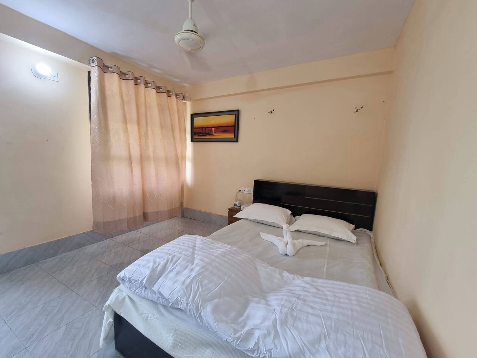 A hotel room with a bed, a nightstand, a painting, and a ceiling fan.