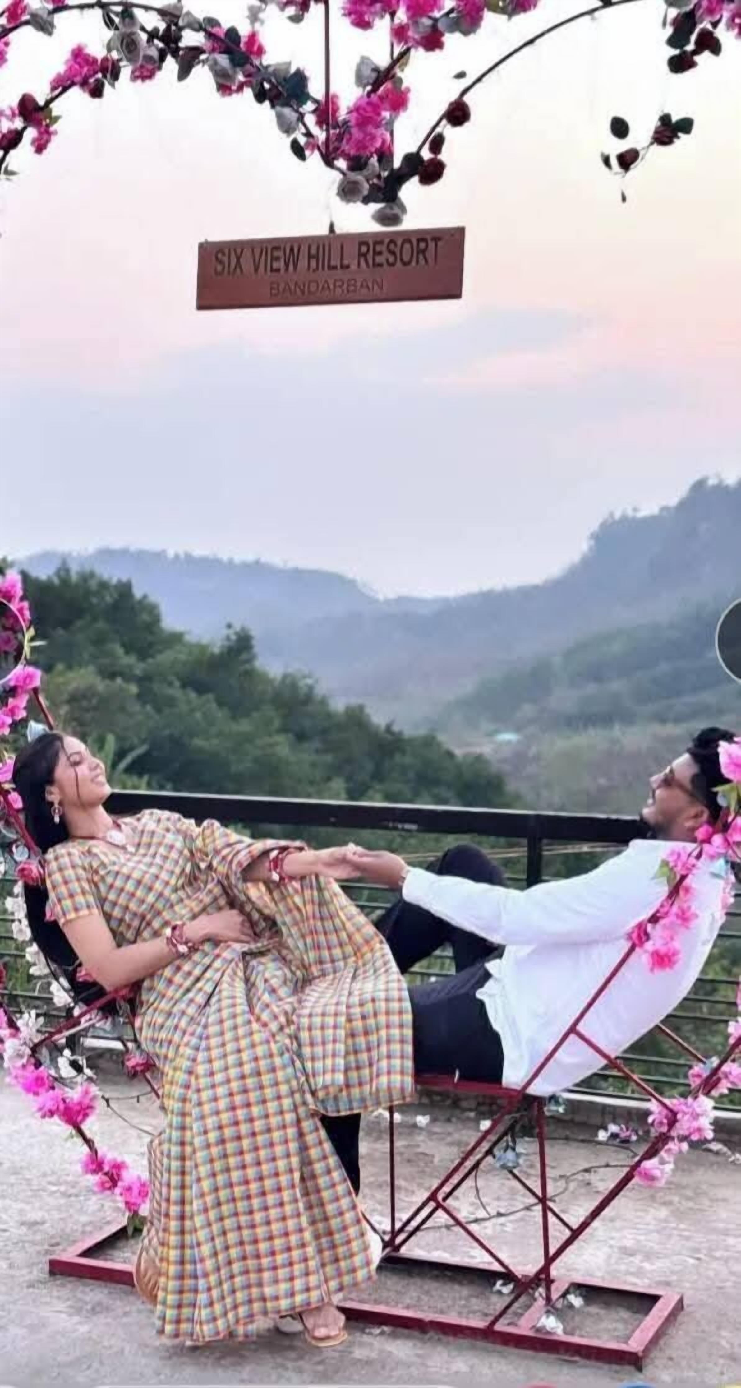 Um casal sentado num baloiço com uma vista panorâmica de colinas ao fundo.
