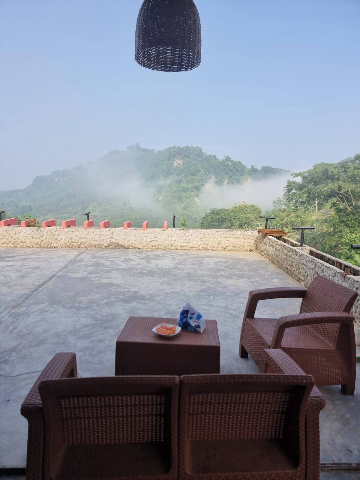 A terrace with wicker furniture, a table with snacks, and a view of mist-covered hills.