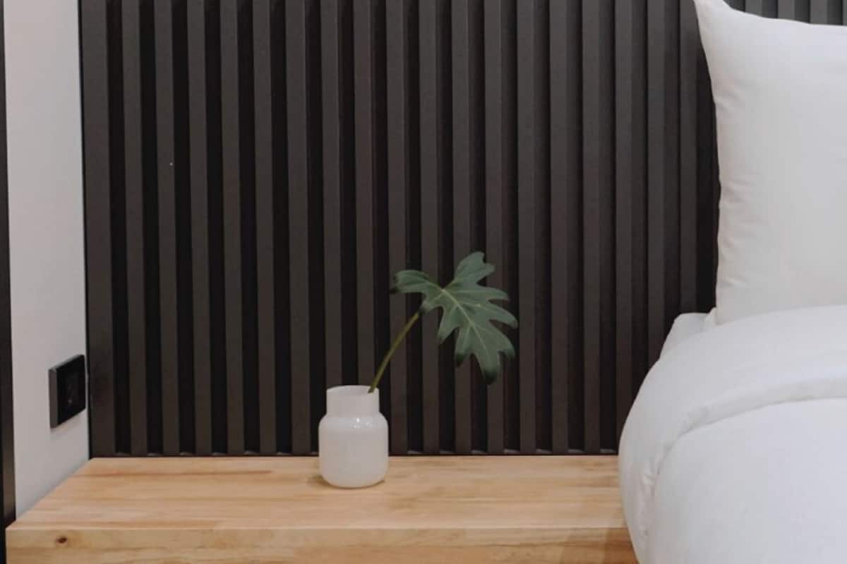 A bedroom with a wooden nightstand, a white vase with a plant, and a bed with white bedding.