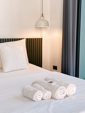 A neatly made bed with white linens and rolled towels, a modern pendant light, and a window with curtains. - Hlangkha Hostel (Betong)