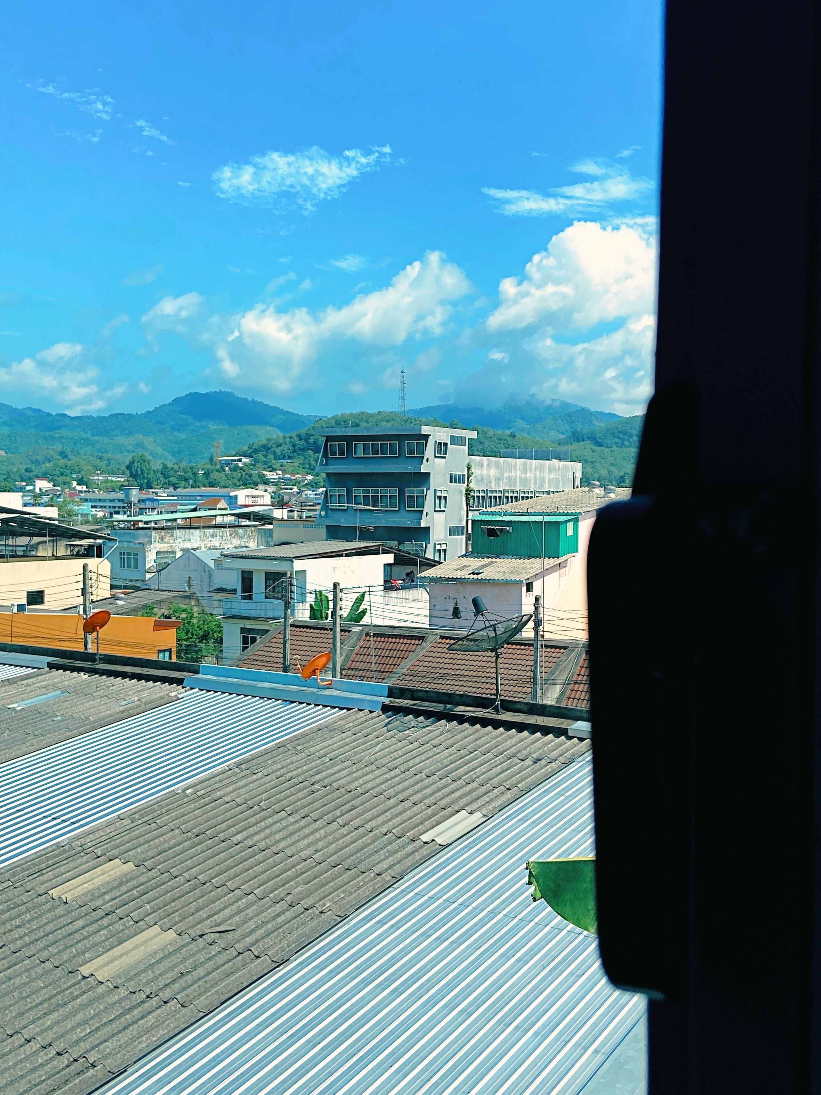 A view of a cityscape with buildings, a prominent multi-story structure, and a mountainous backdrop.