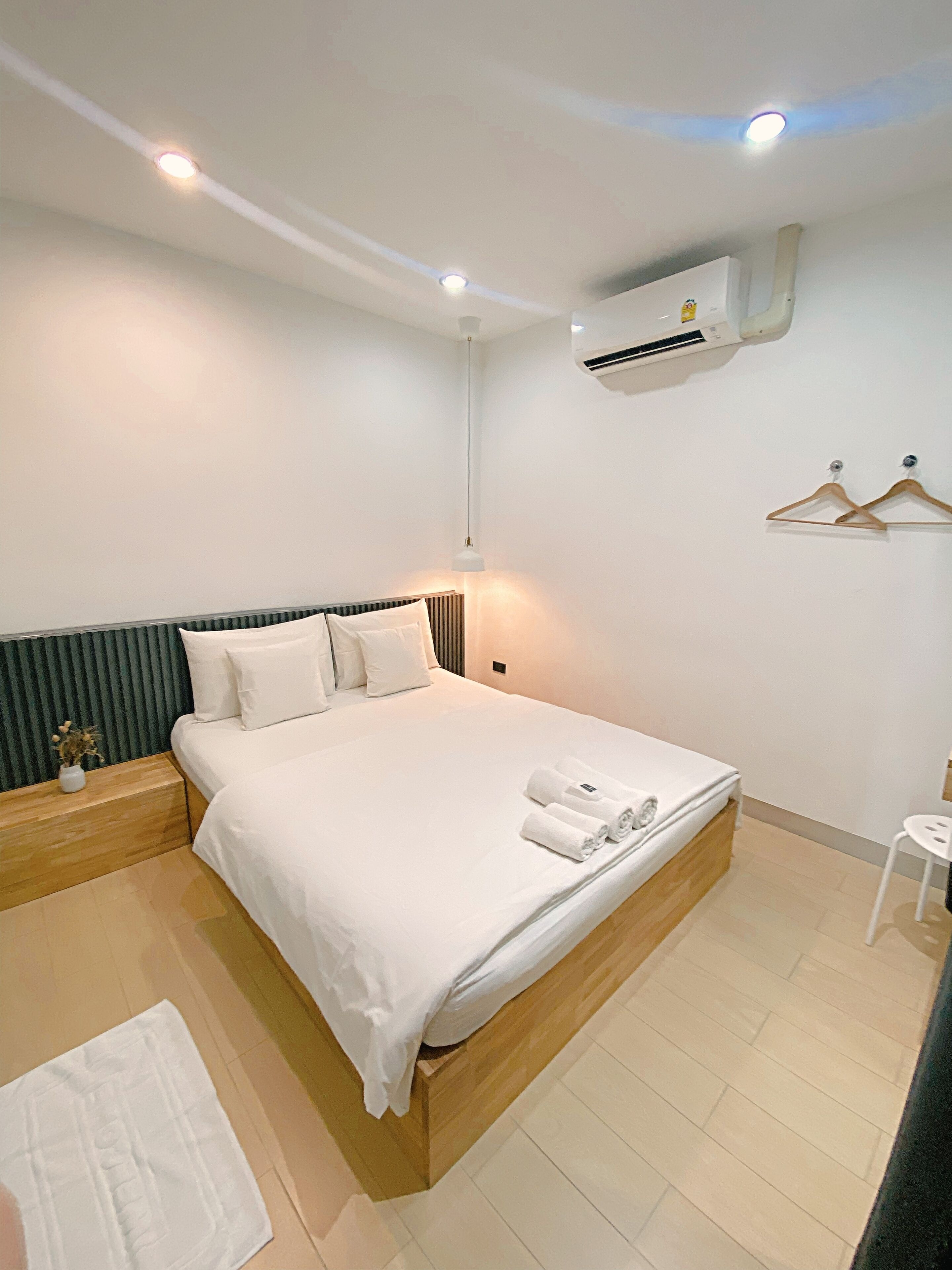 A neatly made bed with white linens, a bedside table with a vase, and a small stool.