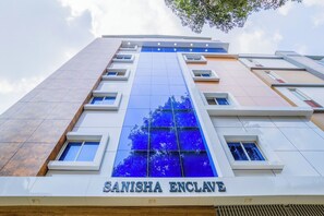 Um edifício moderno com fachada de vidro destacada e o nome "SANISHA ENCLAVE" exibido na parte inferior.