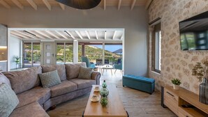 Un salon moderne avec un plafond en bois, un grand canapé, une table basse et une vue sur un paysage montagneux grâce à de grandes fenêtres.
