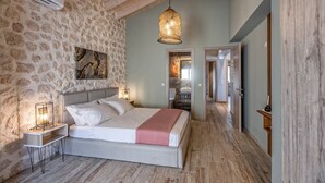 Une chambre avec un mur en pierre, un lit doté d’une tête de lit blanche, un luminaire suspendu et un plancher en bois.
