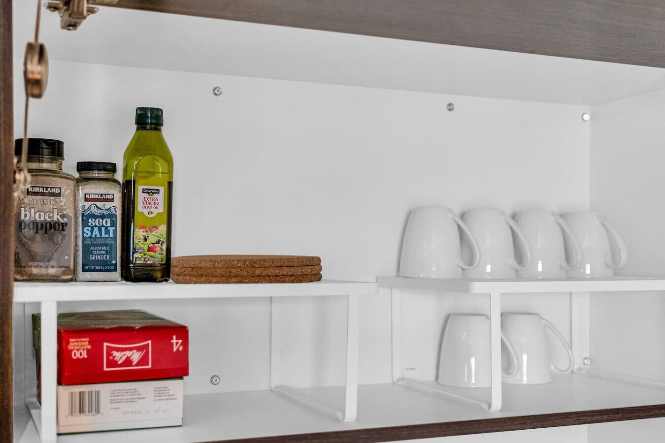 A kitchen area with a white shelf holding a box of coffee, a bottle of olive oil, and jars of spices.