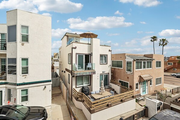 A multi-story residential building with balconies, a patio area with outdoor furniture, and a clear sky.