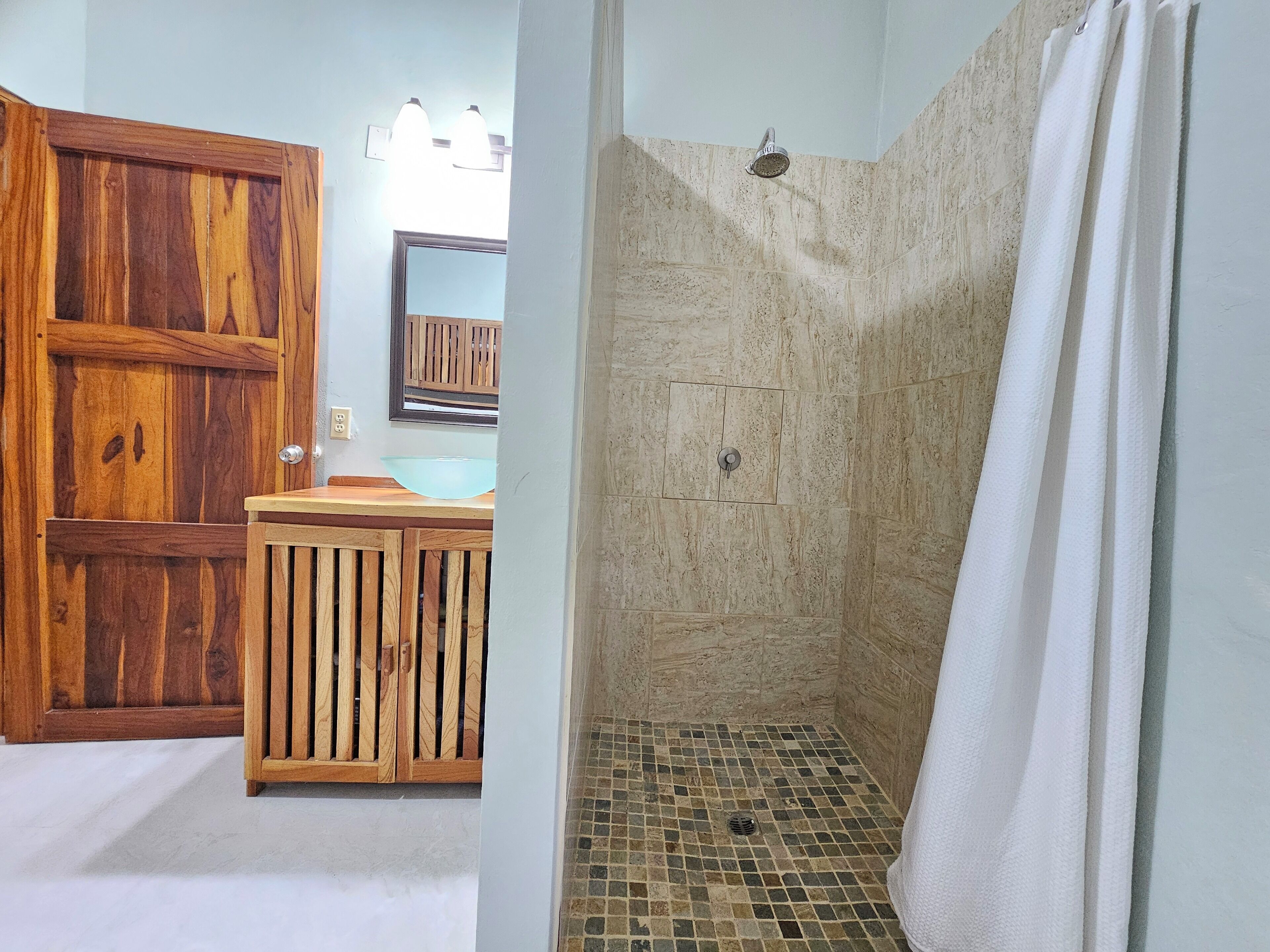 Un baño con un armario de madera, un lavamanos y una ducha con piso de baldosas.
