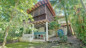 A two-story house with a balcony, surrounded by lush greenery and palm trees. - Pedasi Craftsman Home, Large Screened Deck, Walk to Town (Los Santos Province)